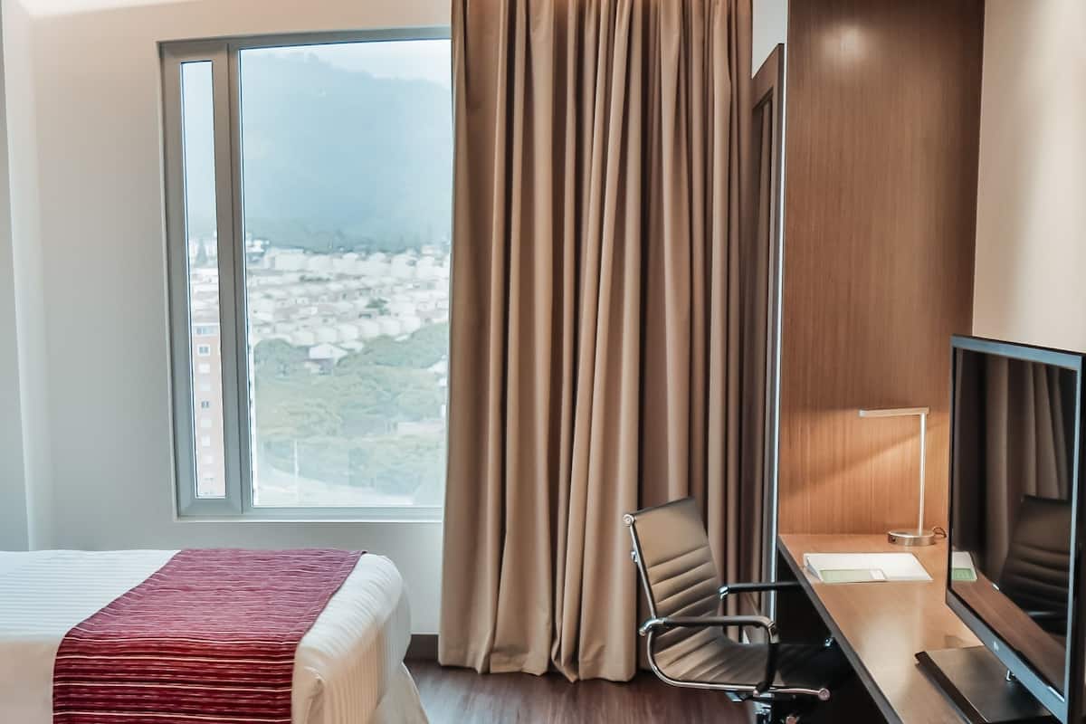 Een hotelkamer met een bed, een bureau, een stoel, een televisie en een raam met gordijnen.