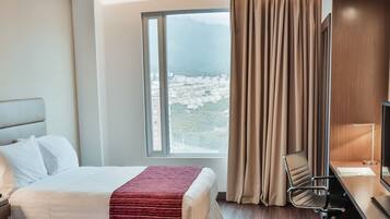 A hotel room with a bed, a desk, a chair, a TV, and a window with curtains.