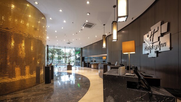 Een moderne hotellobby met een receptiebalie, een Holiday Inn bord en een groot glasraam met uitzicht op het buitenlands gebied.
