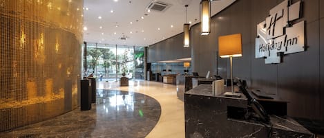 Un moderno vestíbulo de hotel con una mesa de recepción, un letrero de Holiday Inn y un amplio ventanal que ofrece vistas al exterior.