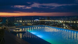 Une vue nocturne d’une piscine, avec les lumières de la ville en arrière-plan.