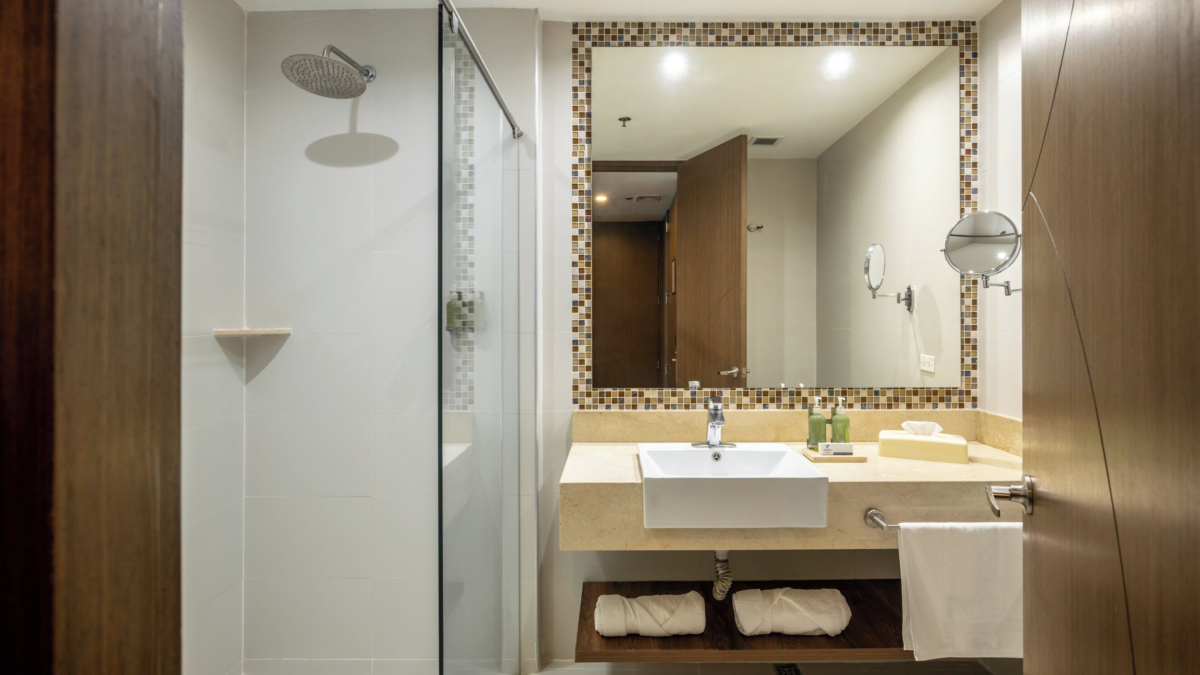 A modern bathroom with a glass-enclosed shower, a sink with a mirror above it, and a wooden vanity with a towel rack.