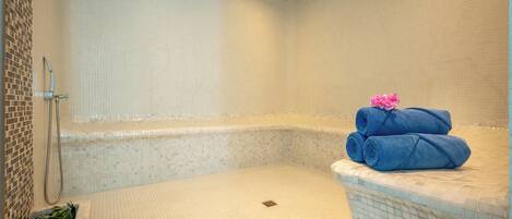 A bathroom with a shower, a tiled floor, and a corner with rolled towels.
