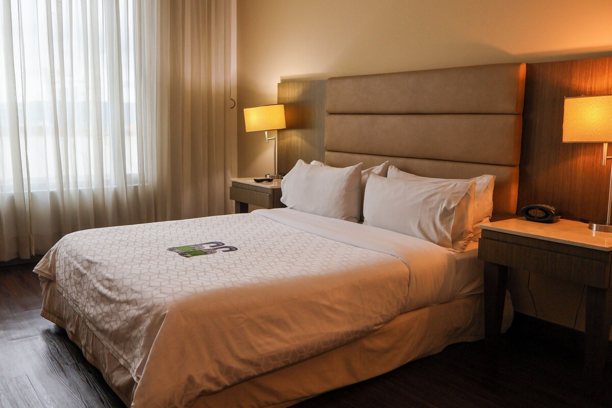 Ein Hotelzimmer mit einem großen Bett, zwei Nachttischen, einer Lampe und einer Uhr.