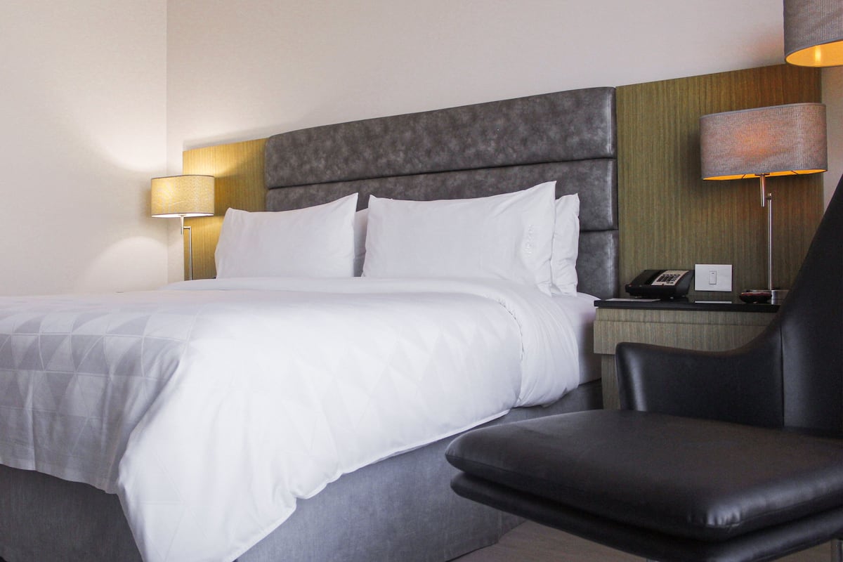 Een hotelkamer met een bed, een stoel, een nachtkastje met telefoon en een lamp.