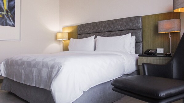 Une chambre d’hôtel avec un lit, une chaise, une table de chevet avec un téléphone et une lampe.