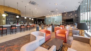 Eine moderne Hotelhalle mit Barbereich, Sitzgelegenheiten und einem großen Fernsehbildschirm.