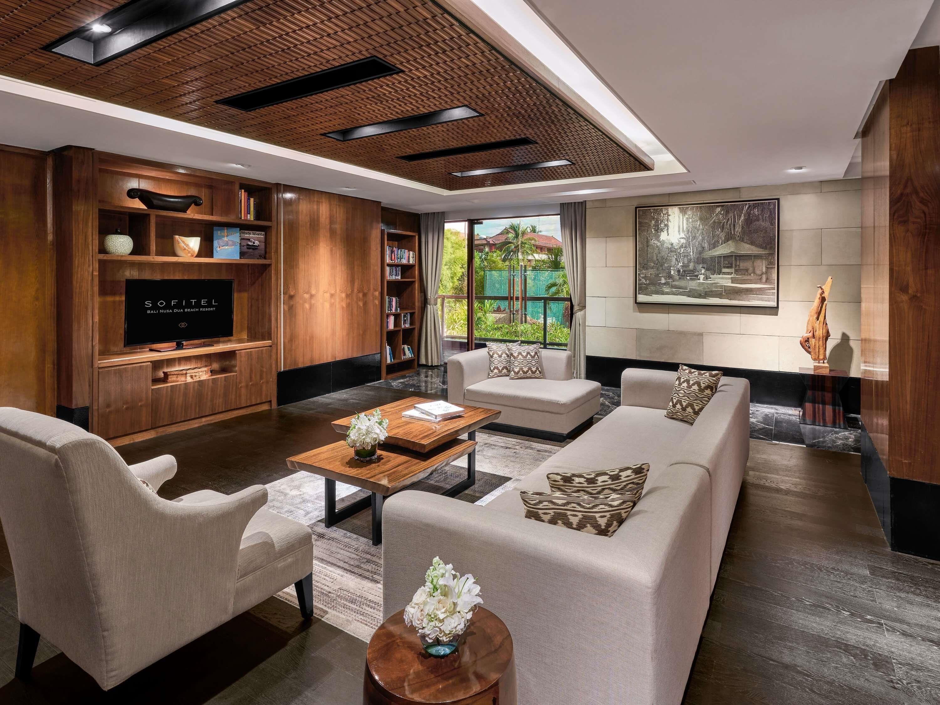 A modern living room with a flat-screen TV, wooden shelving, a sofa, armchairs, and a coffee table.