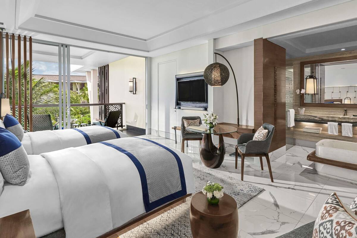 A modern hotel room with a large bed, a seating area with a TV, and a bathroom with a vanity.