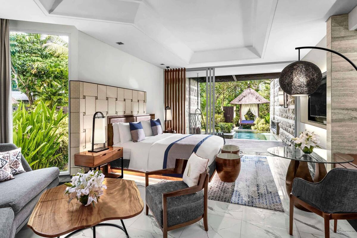 A modern bedroom with a large bed, a glass coffee table, and a view of a swimming pool.