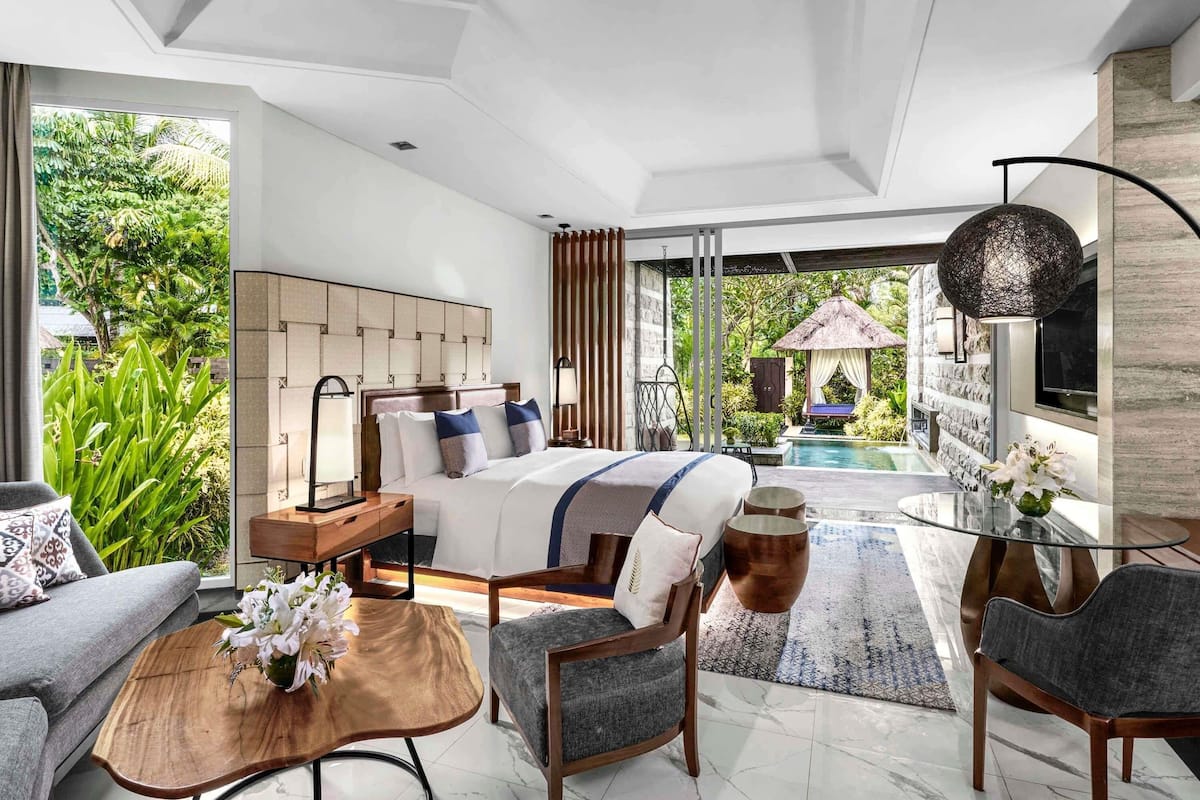 Ein modernes Schlafzimmer mit einem großen Bett, einem Glastisch und Blick auf einen Swimmingpool.
