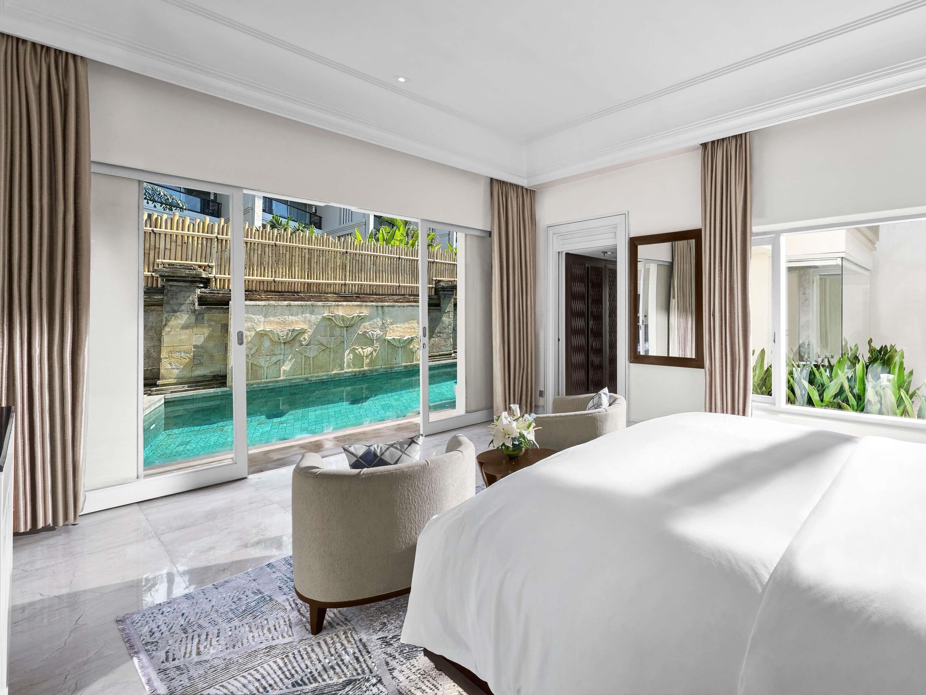 A modern hotel room with a large bed, a view of a pool, and a balcony with a wooden fence.
