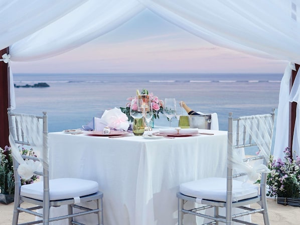 Ein Tisch für zwei Personen mit Blick auf das Meer, weiße Stühle und ein Zelt darüber.