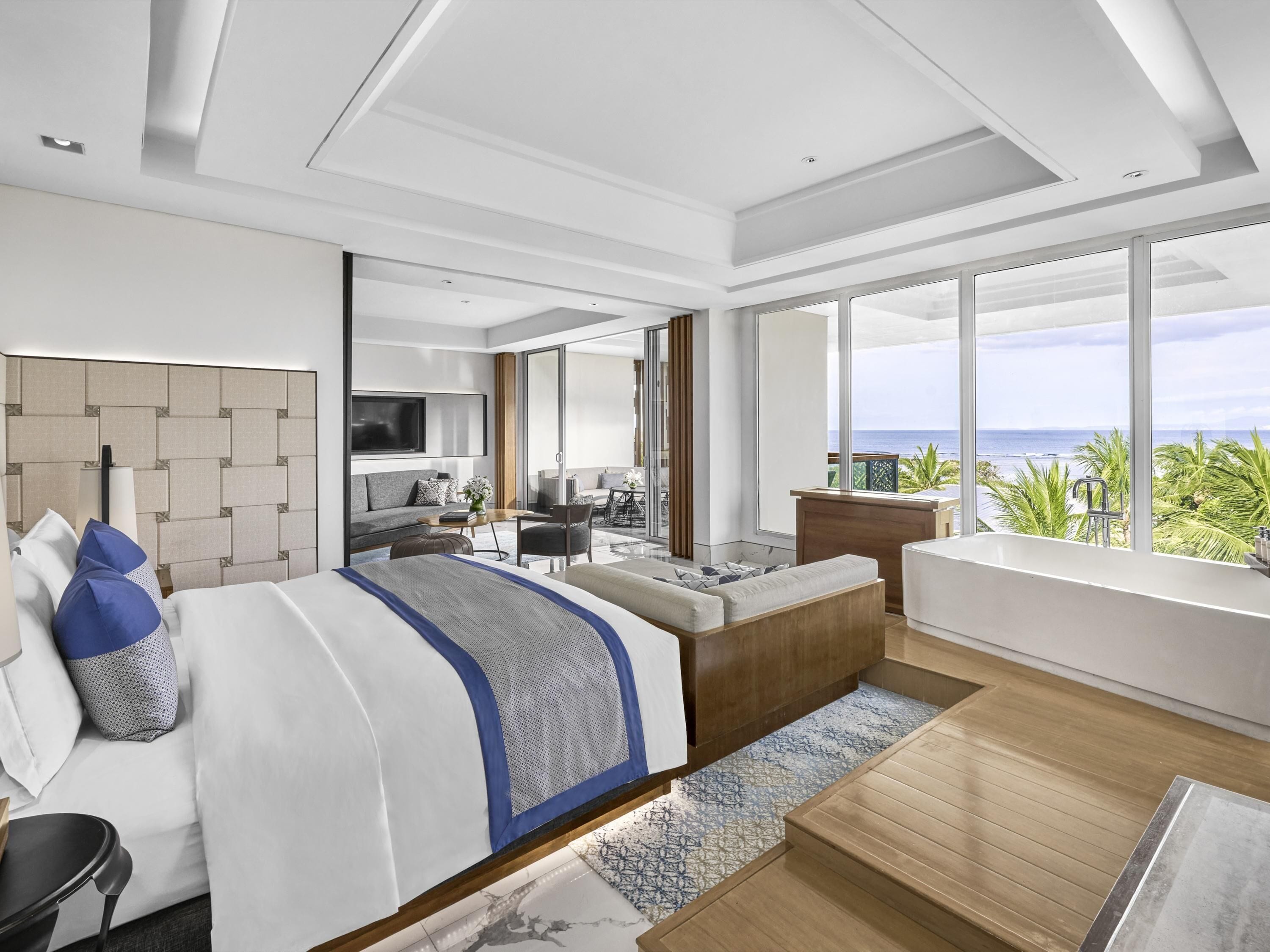 Ein modernes Hotelzimmer mit einem großen Bett, einer Sitzecke, einem Balkon mit Meerblick und einem Fernseher.