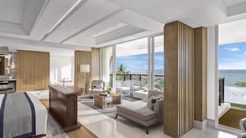 A modern hotel room with a large bed, a desk, a sofa, and a balcony with a view of the sea.
