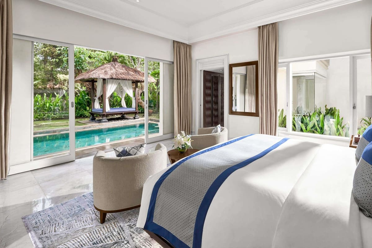 Une chambre spacieuse avec un grand lit, une vue sur une piscine et une structure Ă toit de chaume Ă lâextĂ©rieur.