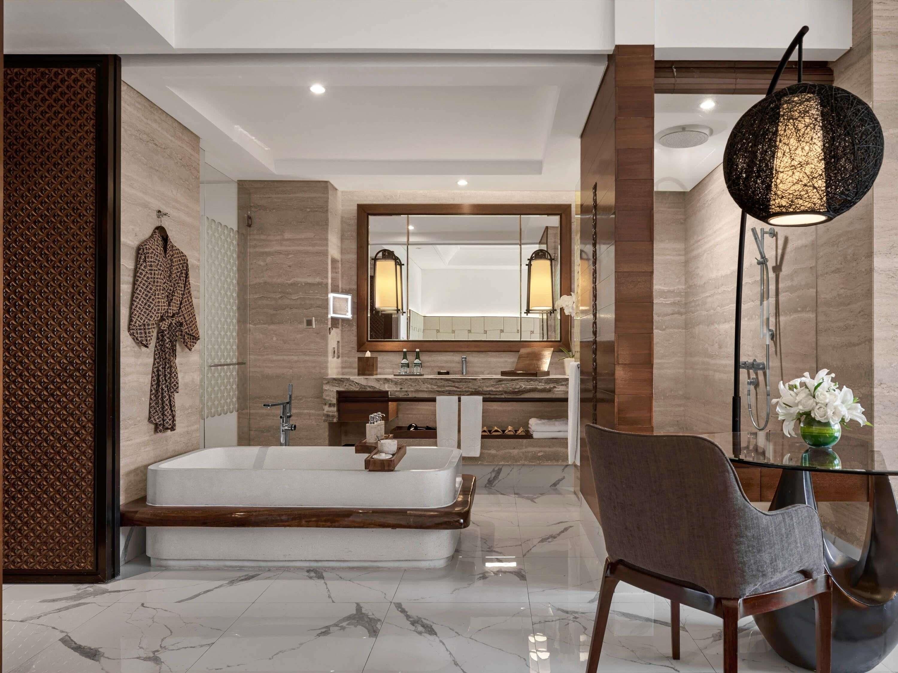 A modern bathroom with a large mirror, a bathtub, a vanity with a marble countertop, and a chair.
