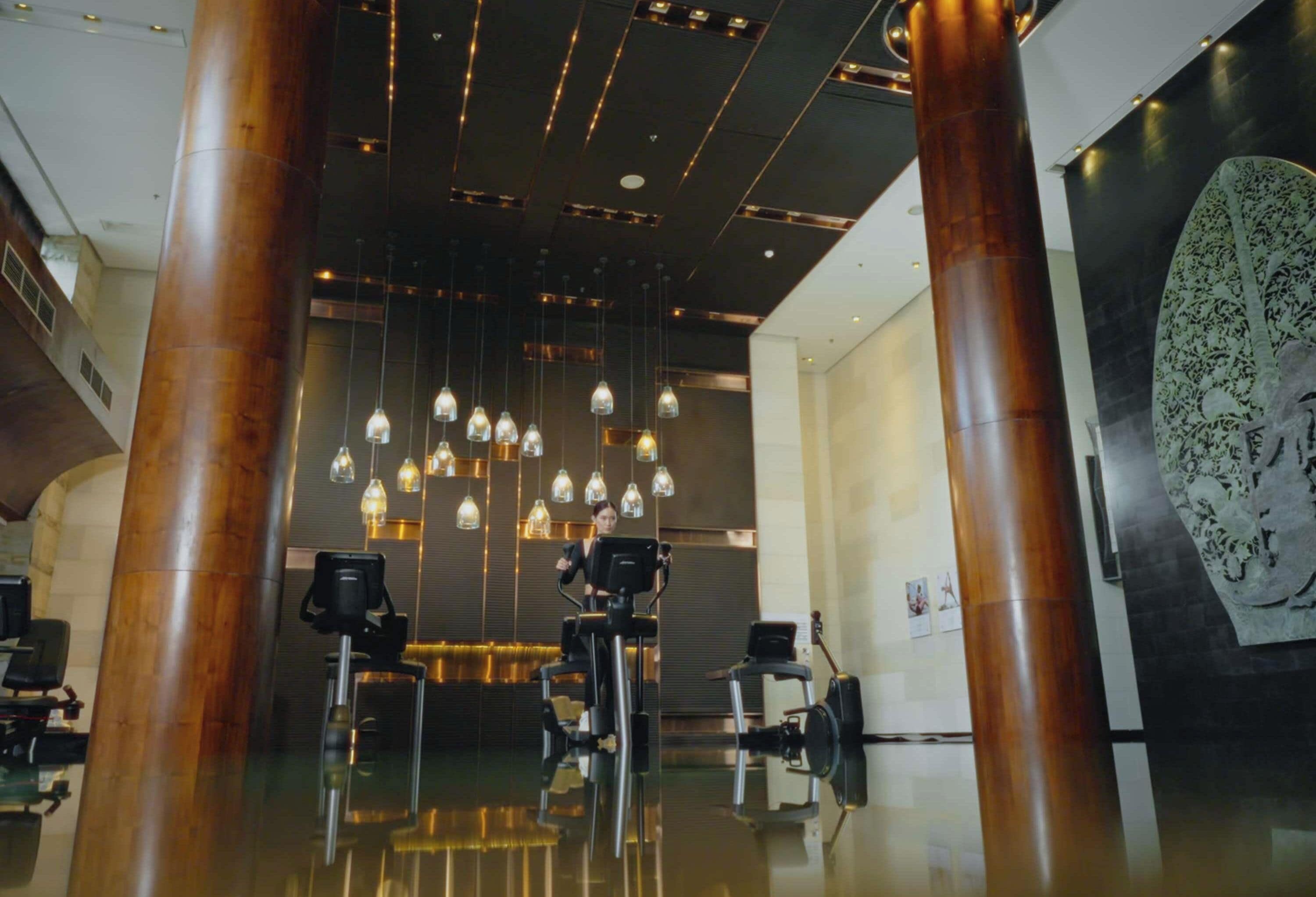 A modern interior with exercise equipment, a large decorative light fixture, and a patterned wall.