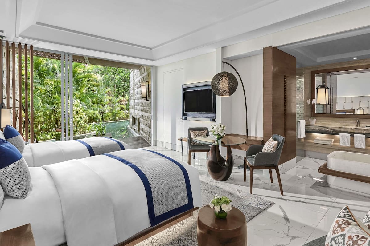 Une chambre d’hôtel moderne dotée d’une grande fenêtre, d’un téléviseur à écran plat, d’un coin repas et d’une salle de bain avec un plan de toilette en marbre.