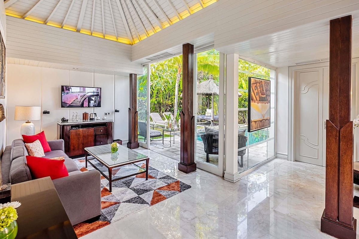 A spacious living area with a large TV, comfortable seating, a glass door leading to a pool, and a modern ceiling design.
