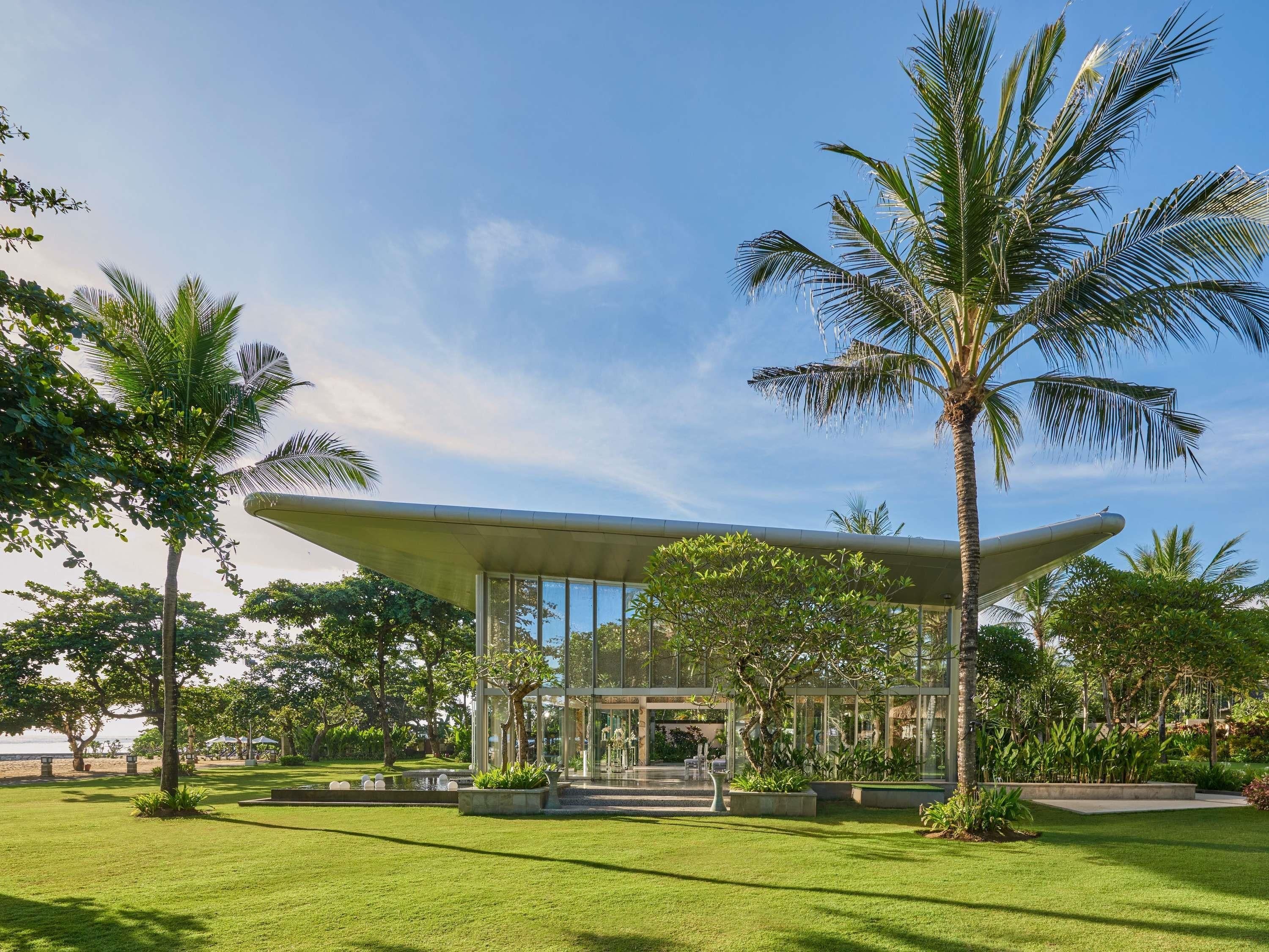 A modern building with a glass facade, surrounded by a well-maintained lawn and palm trees.