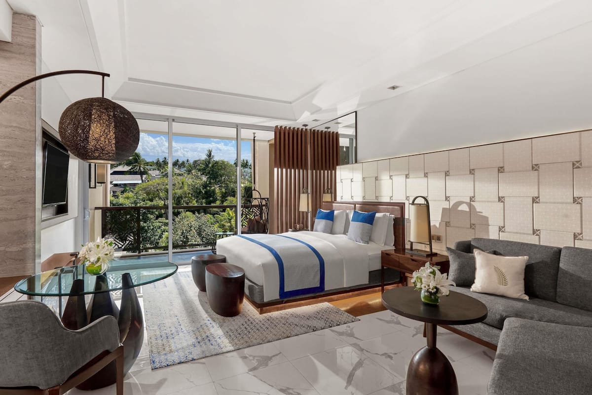 Ein modernes Hotelzimmer mit einem großen Bett, einem Sofa, einem Glastisch und einem Balkon mit Blick.