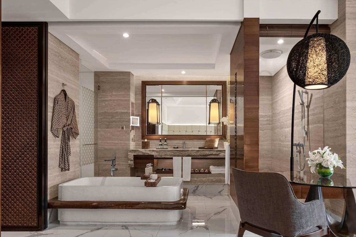 A modern bathroom with a large mirror, a bathtub, a vanity with a marble countertop, and a chair.