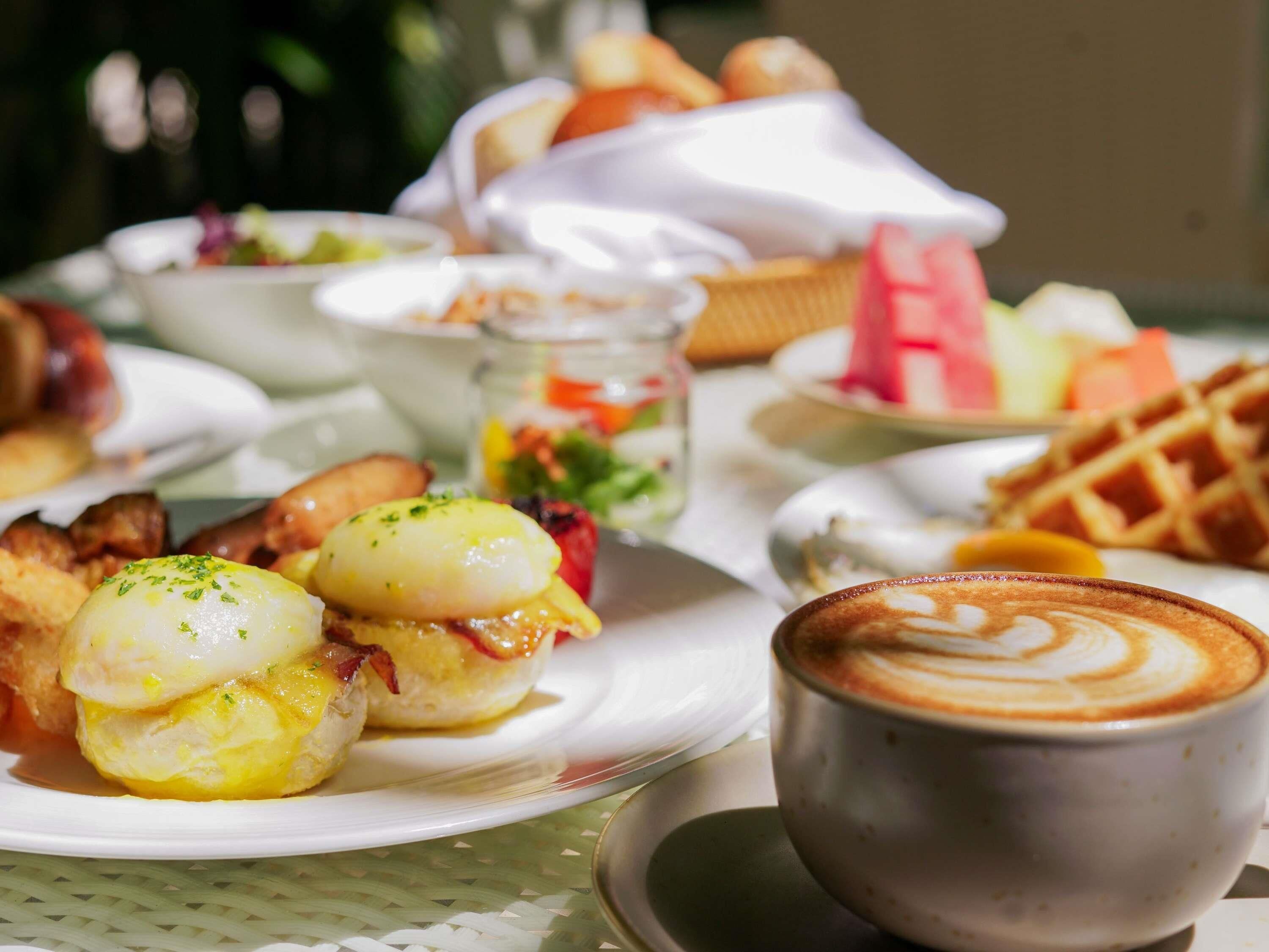 Une table dressée pour le petit-déjeuner, avec des assiettes remplies de nourriture, une tasse de café et un gaufre.