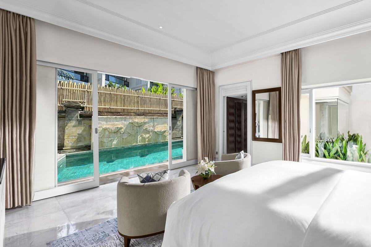 A modern hotel room with a large bed, a view of a pool, and a balcony with a wooden fence.