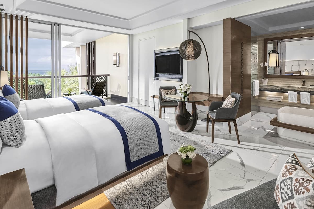 Une chambre d’hôtel moderne équipée de deux lits, d’un coin repas, d’une télévision et d’une salle de bain.