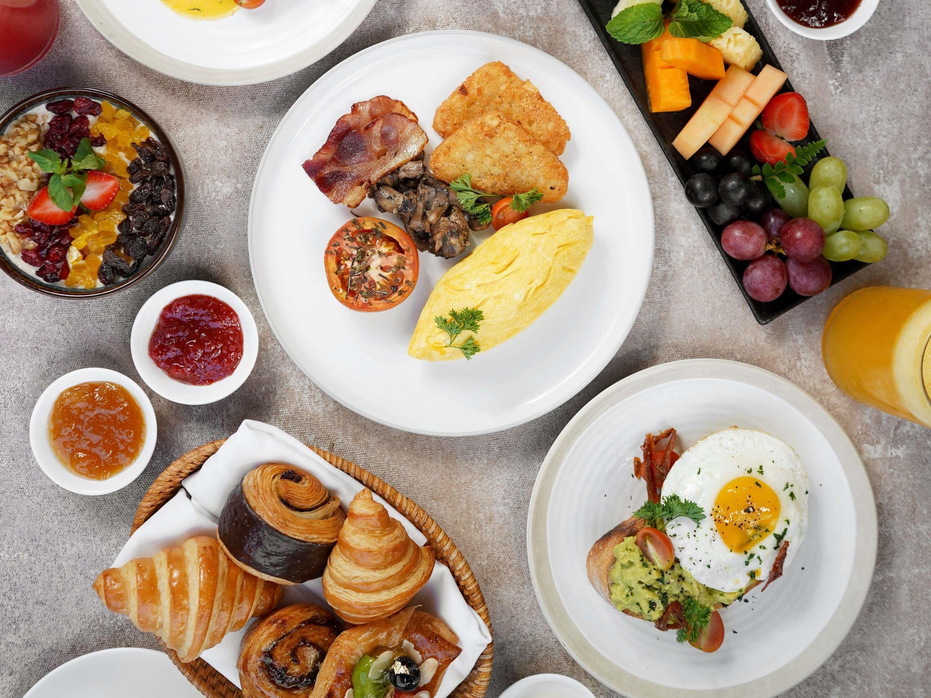 Una mesa de desayuno con varios platos, incluyendo huevos, tocino y pastelería.