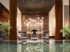 Un hall d’hôtel moderne doté d’un espace salon central, d’équipements de fitness et d’un grand miroir qui reflète l’ensemble de l’espace.