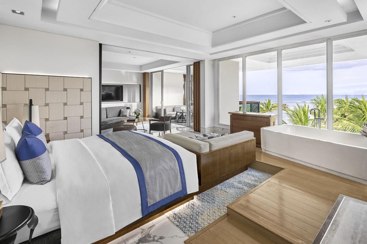 Une chambre d’hôtel moderne dotée d’un grand lit, d’un coin salon, d’un balcon avec vue sur l’océan et d’une télévision.