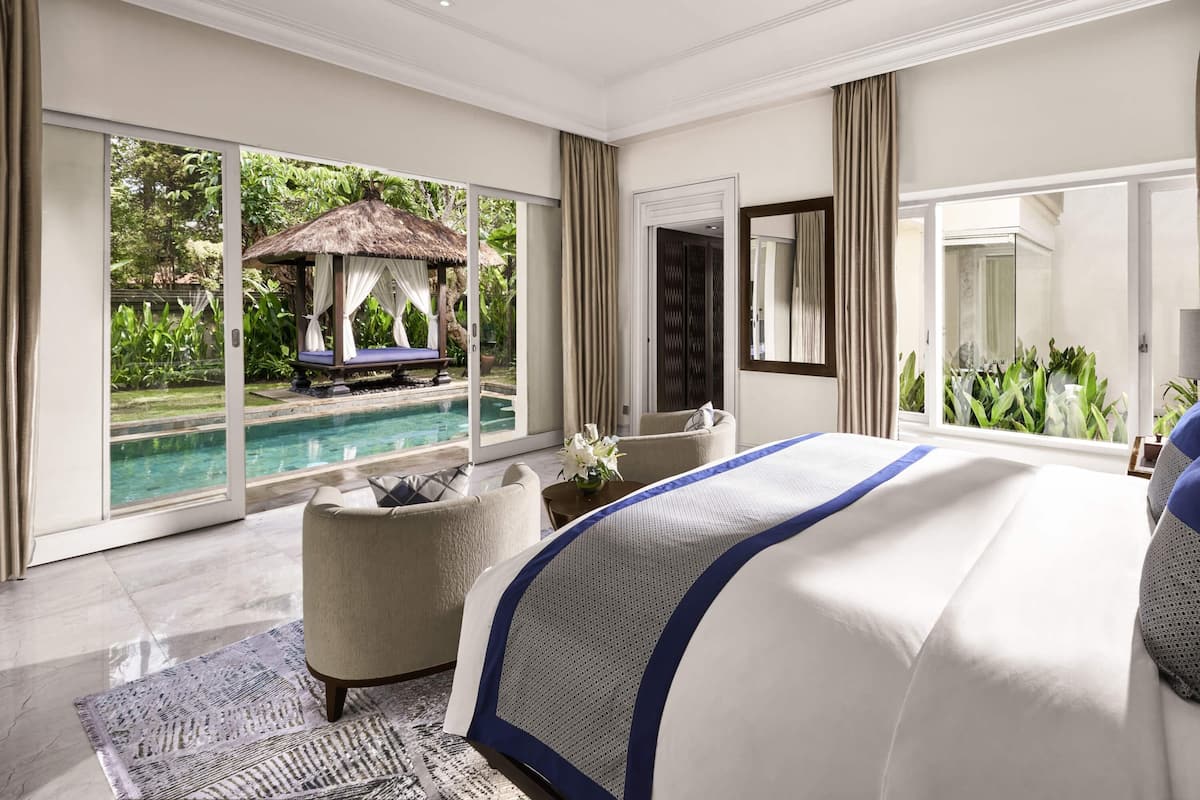 Une chambre dotée d’un grand lit, d’un coin salon, d’une vue sur une piscine à débordement et d’une structure à toit de chaume.