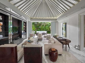 A modern living room with a large TV, comfortable seating, a coffee table, and a view of lush greenery outside. - Sofitel Bali Nusa Dua Beach Resort (Nusa Dua)