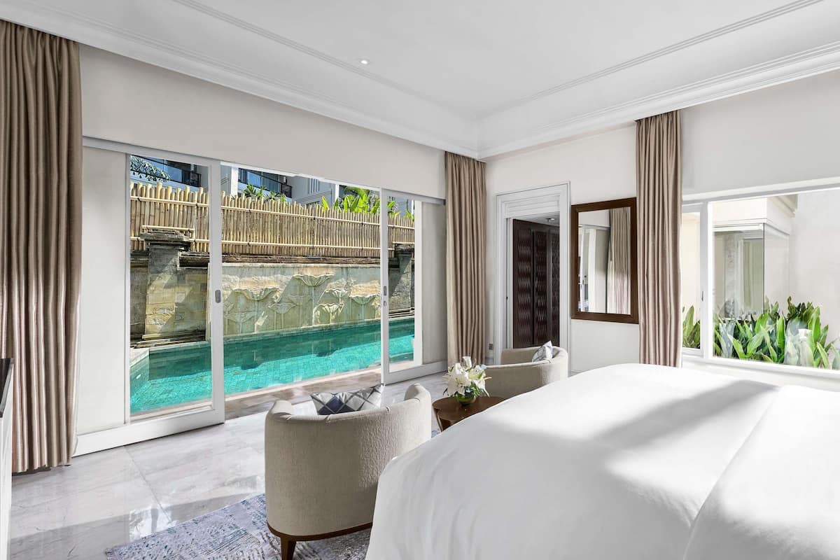 A modern hotel room with a large bed, a view of a pool, and a balcony with a wooden fence.