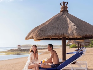 A beach scene with a thatched umbrella, lounge chairs, and a calm sea. - Sofitel Bali Nusa Dua Beach Resort (Nusa Dua)