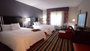 Habitación de hotel con dos camas, un escritorio, un televisor y una ventana con cortinas.
