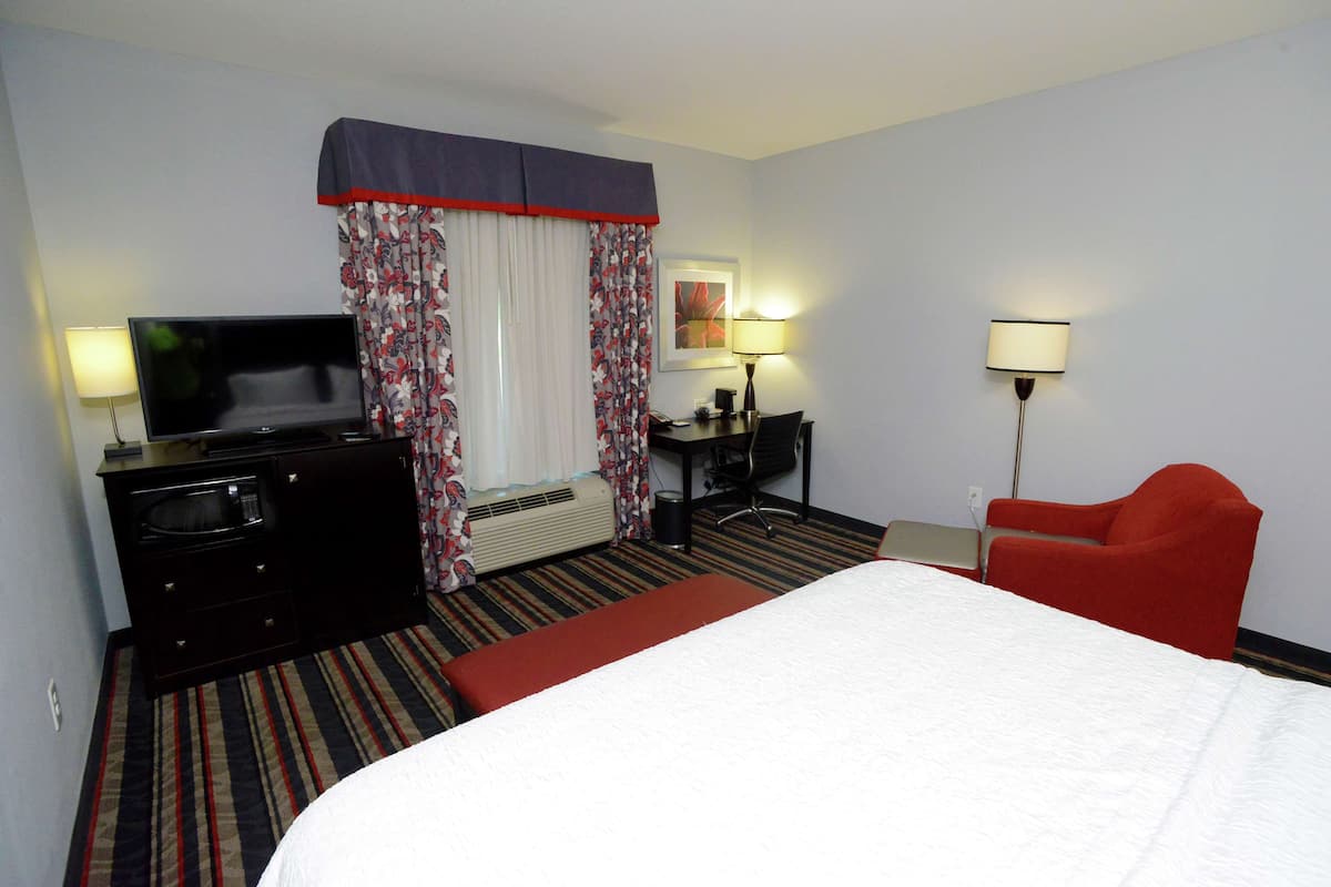 A hotel room with a bed, a desk with a computer, a television, and a red armchair.
