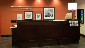 A reception desk with framed photos, a sign reading "welcome to Albany," and a vending machine.