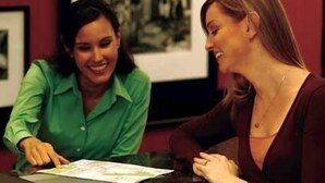 Dos personas sentadas a una mesa con un mapa, en una habitación con cuadros en la pared.