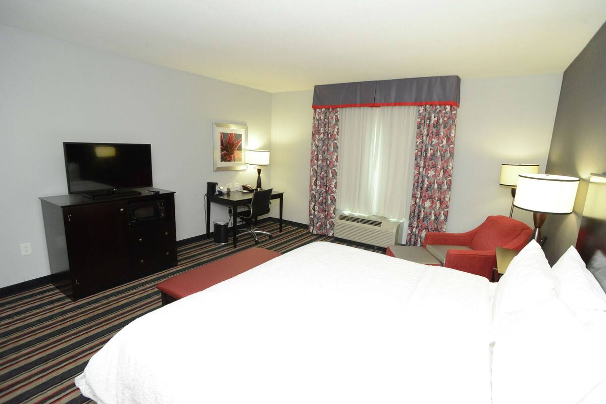 A hotel room with a bed, a desk with a chair, a television, and a window with curtains.