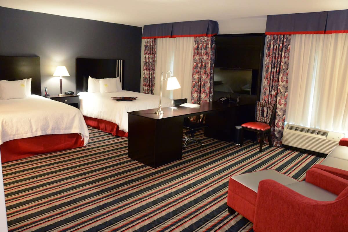 A hotel room with two beds, a desk, a chair, a TV, and a red sofa.