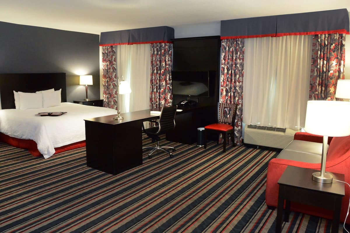 A hotel room with a bed, desk, chair, and a TV.