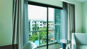 A hotel room with a large window, a balcony, and a view of buildings and greenery. - Widus Hotel Clark (Mabalacat City)