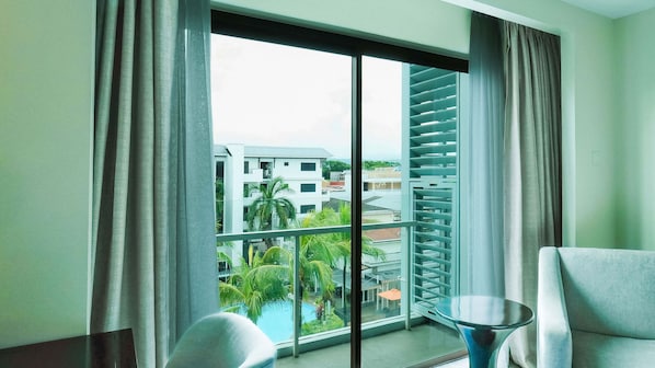A hotel room with a large window, a balcony, and a view of buildings and greenery. - Widus Hotel Clark (Mabalacat City)