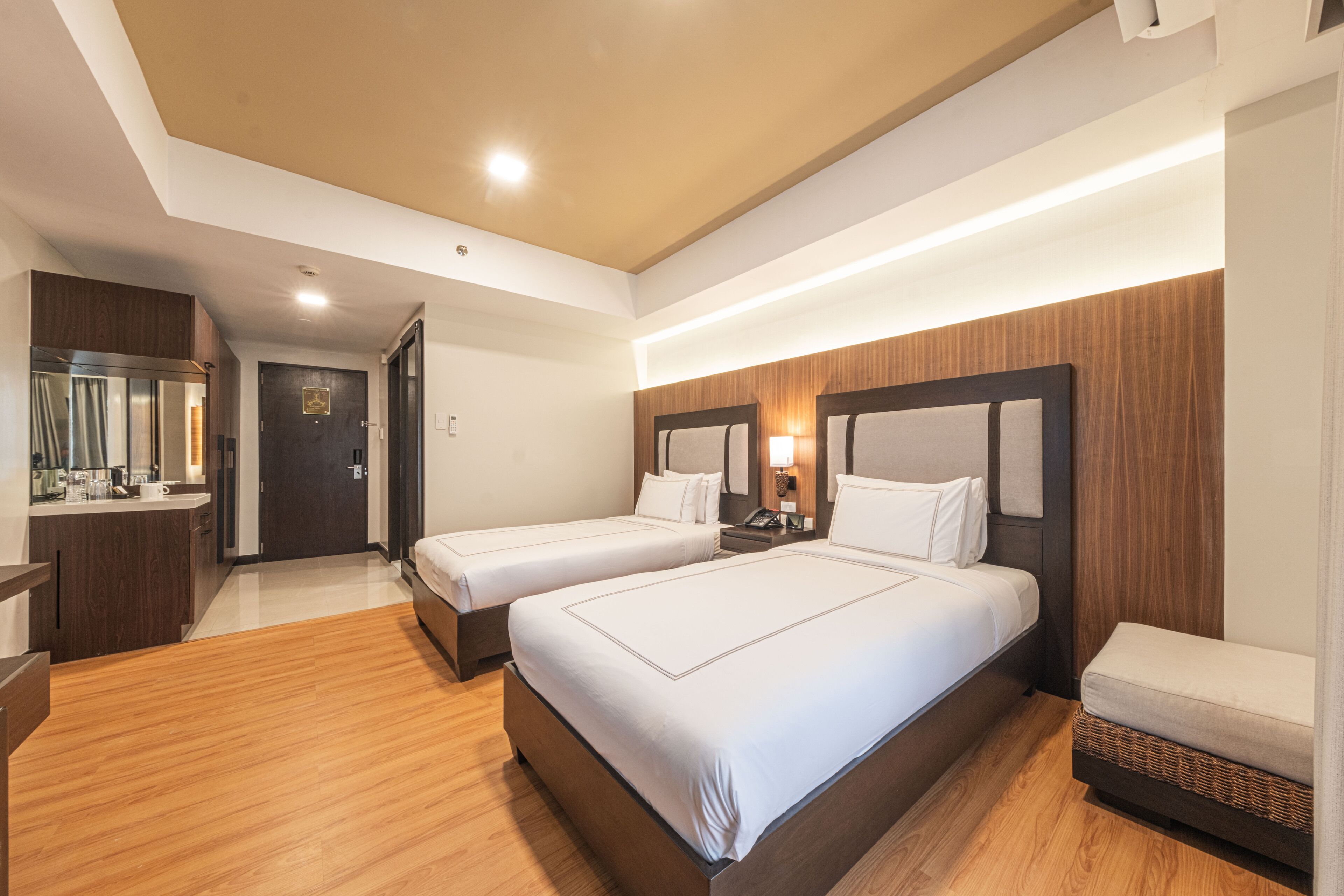 Habitación de hotel con dos camas, piso de madera, escritorio con espejo y baño visible a través de una puerta abierta.