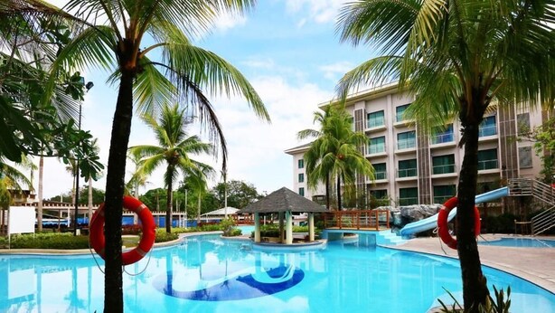 A swimming pool with palm trees, lifebuoys, and a building in the background. - Widus Hotel Clark (Mabalacat City)
