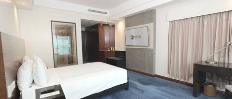 A hotel room with a bed, a desk, a chair, a TV, and a bathroom door.