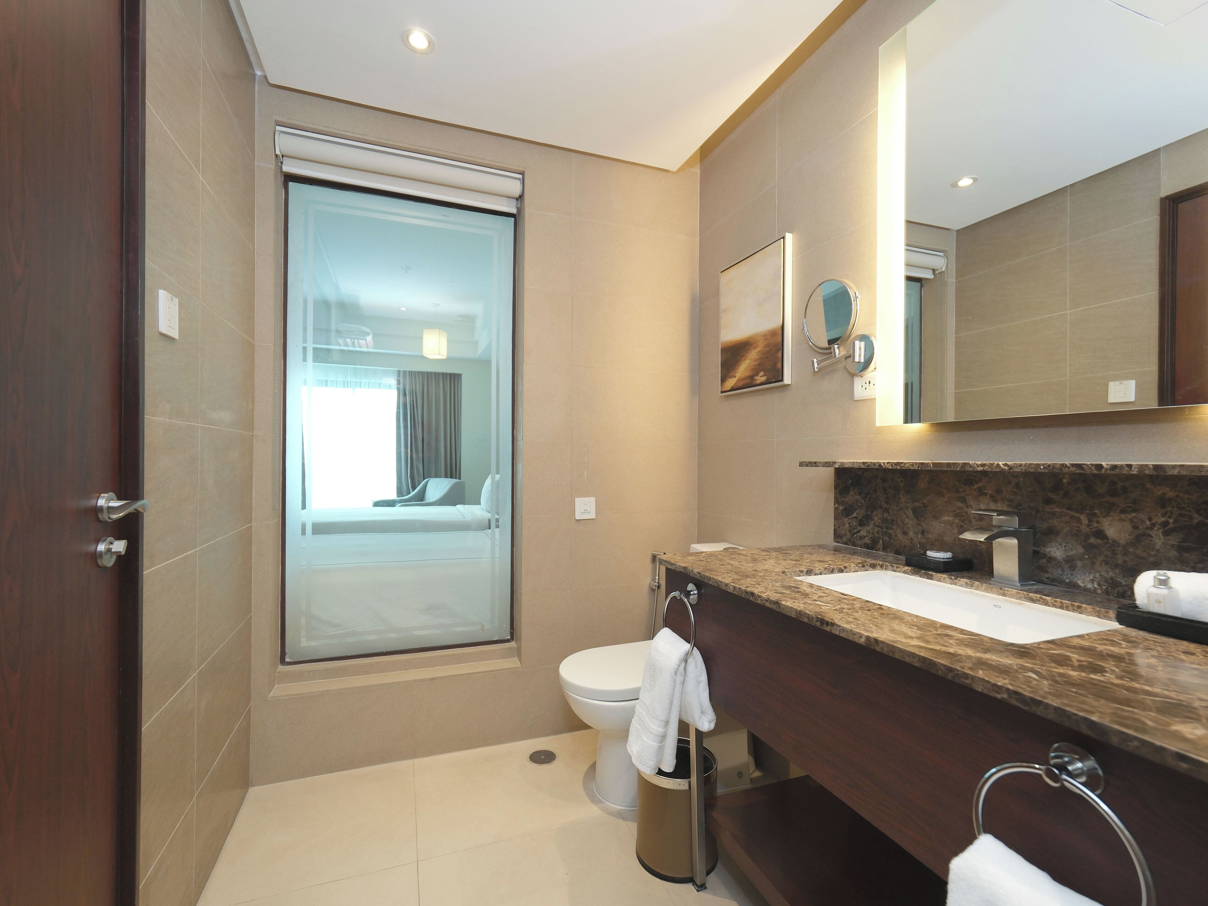 A modern bathroom with a marble countertop, a toilet, and a glass door leading to a bedroom.